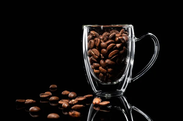 Coffee bean in a glass cup, coffee beans are scattered nearby. side view on black background — Stock Photo, Image