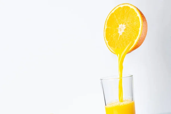 Fresh orange juice is poured from half an orange into a transparent glass. place for inscription — Stock Photo, Image