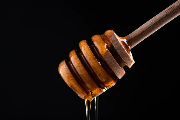 Fresh honey flows from a wooden spoon for honey close-up on a black background — Stock Photo, Image