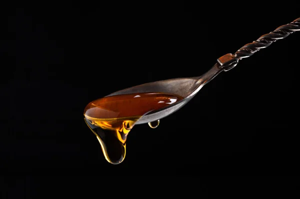 Honey flows from a carved vintage silver spoon on a black background close-up — Stock Photo, Image