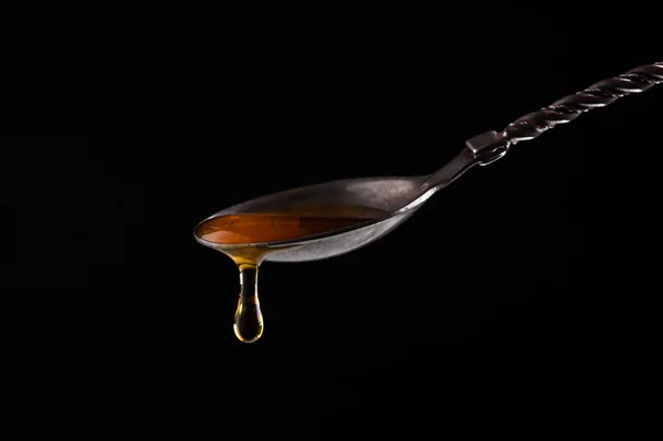 Honey pours from a vintage silver spoon on a black background close-up — Stock Photo, Image