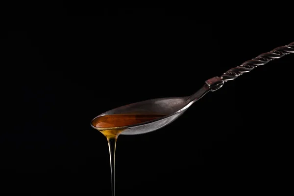 Honey pours from a vintage silver spoon on a black background close-up — Stock Photo, Image