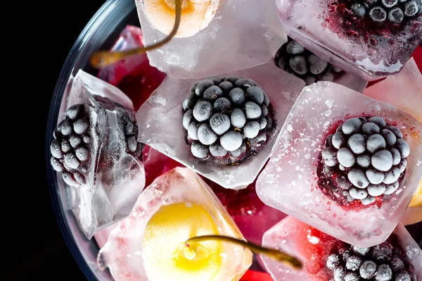 Gefrorene Himbeeren Beeren Kirschen und Brombeeren in Eisstücken in einer Glasschüssel auf schwarzem Hintergrund — Stockfoto