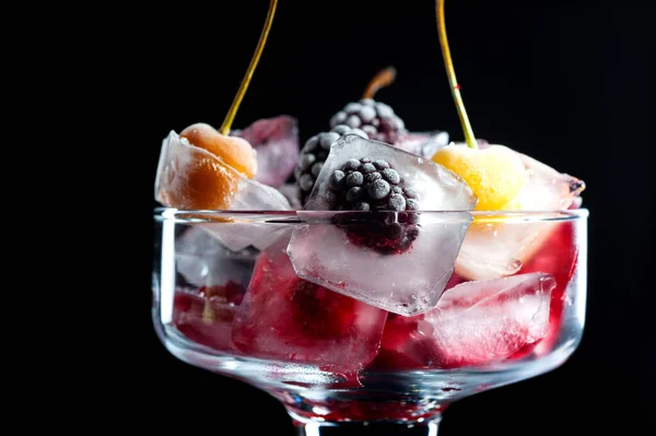 Замороженные ягоды малины вишни и ежевики в кусках льда в стеклянной чаше на черном фоне — стоковое фото