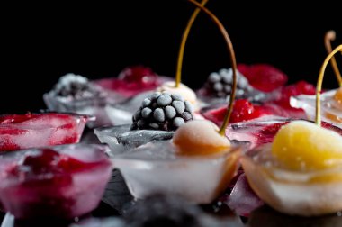  Donmuş ahududu kirazları ve böğürtlenler siyah arka planda cam bir kasede buz parçalarındalar.