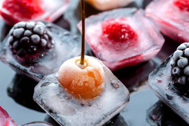  Donmuş ahududu kirazları ve böğürtlenler siyah arka planda cam bir kasede buz parçalarındalar.