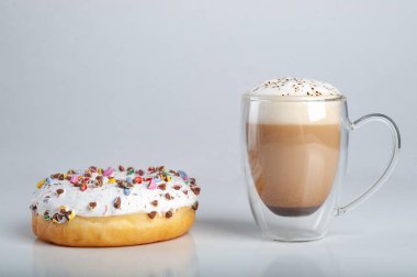 Köpüklü kapuçino, şeffaf bir bardakta, beyaz arka planda taze bir çöreğin yanında, çift tabanlı, şeffaf bir bardakta.