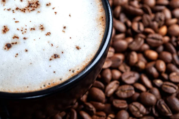 Une tasse noire de café noir avec un gros plan en mousse blanche, se tient sur une table où les grains de café sont dispersés. plan supérieur copyspace — Photo