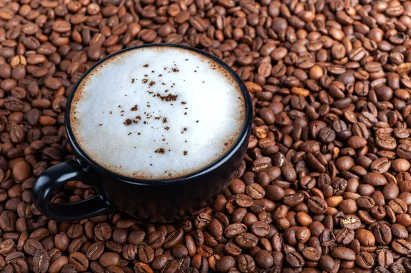 Uma xícara preta de café preto com espuma branca está na mesa onde os grãos de café estão espalhados. espaço copyspace tiro superior — Fotografia de Stock