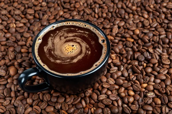 Uma xícara preta de café preto fica em uma mesa onde os grãos de café estão espalhados. espaço de cópia — Fotografia de Stock