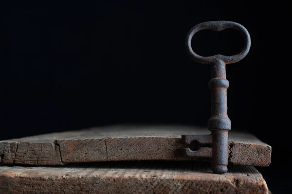 Three old rusty keys stand on old wooden board against a dark background — Stock Photo, Image