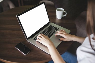 Mockup görüntüsünü kullanarak ve boş beyaz ekran ve modern loft kafede masada kahve fincanı ile laptop yazarak iş kadını