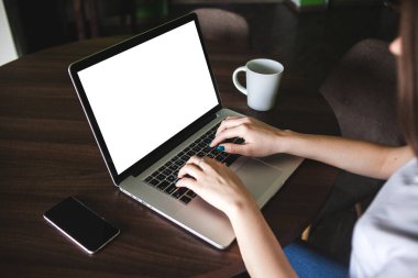 Mockup görüntüsünü kullanarak ve boş beyaz ekran ve modern loft kafede masada kahve fincanı ile laptop yazarak iş kadını