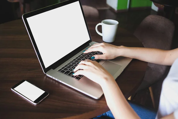 Mockup görüntüsünü kullanarak ve boş beyaz ekran ve modern loft kafede masada kahve fincanı ile laptop yazarak iş kadını