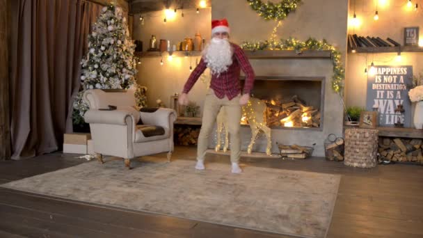 Roliga jultomten dansar mot en öppen spis och en julgran — Stockvideo
