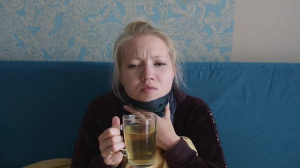 Jovem mulher está doente e bebe chá quente senta-se no sofá — Vídeo de Stock