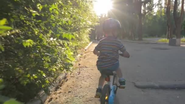 Küçük mavi kasklı çocuk gün batımında bisiklete biniyor ya da gün doğumunda parkta — Stok video