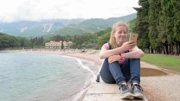 Красива молода жінка сидить на парапеті зі смартфоном — стокове відео