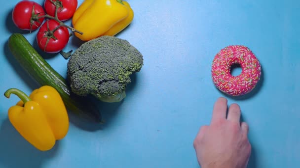 Чоловіча рука хоче взяти рожевий пончик, але вирішує взяти свіжий брокколі — стокове відео