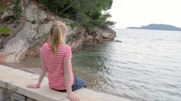 Chica sentada en el parapeto mirando al mar — Vídeos de Stock