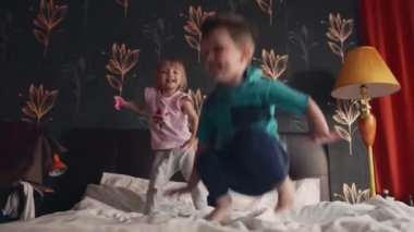 Erkek ve kız kardeşler, anne babalarının yatak odasında çift kişilik yatakta zıplıyorlar.
