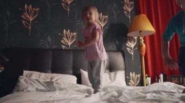 İki neşeli kız ve erkek kardeş eğleniyor ve çift kişilik yatakta zıplıyorlar. 