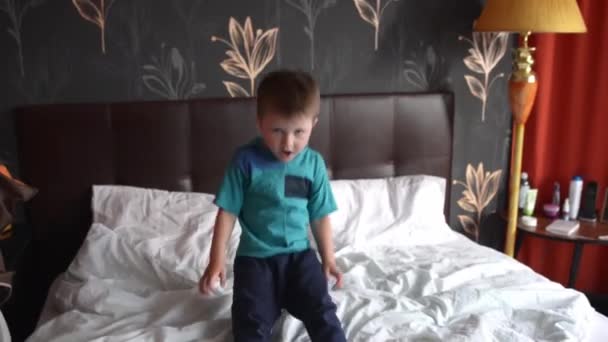 Klein gelukkig kind jongen vallen op een zacht groot bed met witte kussens — Stockvideo