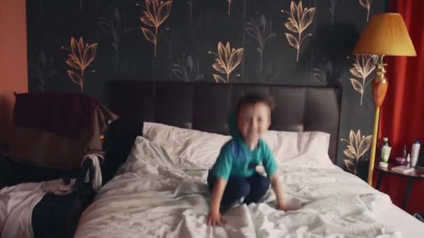 Мальчик прыгает в высоту на двуспальной кровати родителей, как на батуте — стоковое видео
