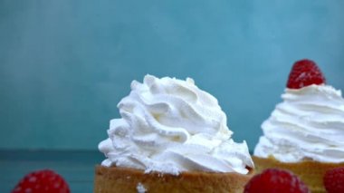 Children hand puts raspberry on a meringue cake on blue background