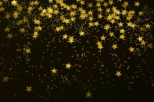 gold star confetti and glitter on a black background - Christmas / New Year party festive backdrop for your projects - selective focus