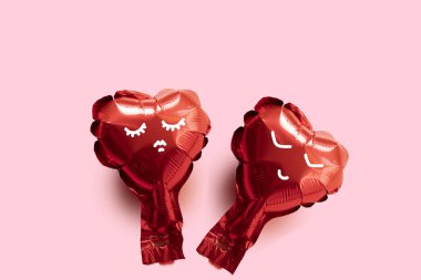 Pembe arka planda yüzü olan iki kırmızı folyolu balon kalp Sevgililer Günü kartı.
