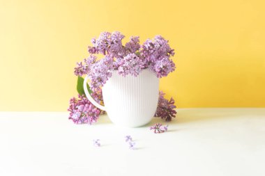 Sarı arka planda leylak çiçekli beyaz bardak.