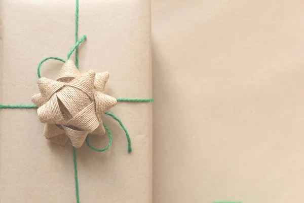 Regalo avvolto in carta riciclata semplice con filo verde su sfondo beige — Foto Stock