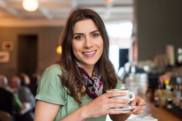 Flicka på coffe shop håller en kopp och ler mot kameran. — Stockfoto