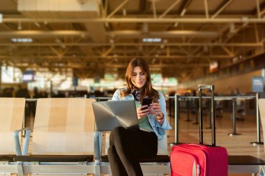 Kadın yolcu terminal salonda oturmuş laptop ve akıllı telefon