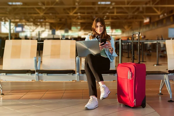 Kobiece pasażera na inteligentnego telefonu i laptopa siedząc w hali terminala — Zdjęcie stockowe