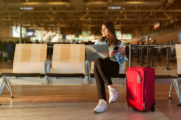 Passeggero su smartphone e laptop seduto nella hall del terminal dell'aeroporto — Foto Stock