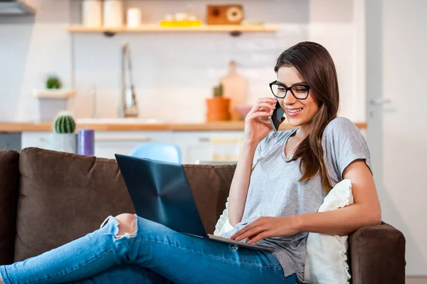 Mujer usando portátil y teléfono celular tumbado en el sofá —  Fotos de Stock