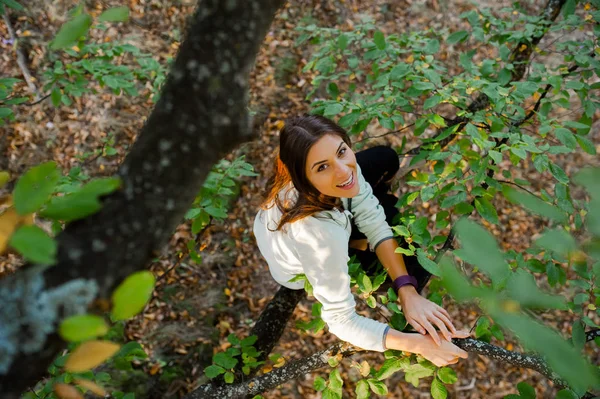 Kvinna sitter i ett träd tittar på kameran och leende. — Stockfoto