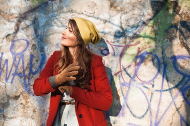 Grafiti duvarı günbatımı güneş altında dinlenmek için bir an sahip şık Kabanlar giyen genç kız sonbahar şehirde.