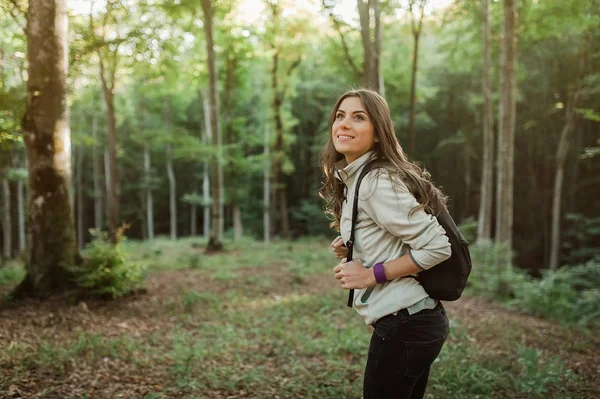 Kamera bir sırt çantası ormanda günbatımı ışık sonbahar sezonunda mutlu gülümseyen genç ve güzel kadın.