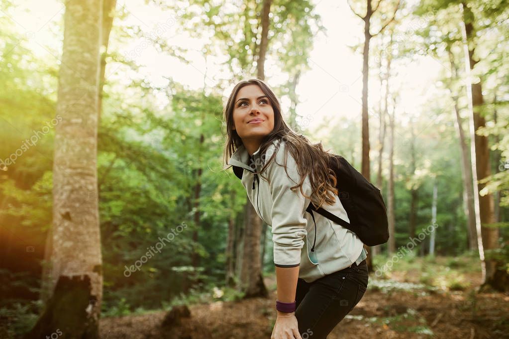 Young woman resting after a walk in the forest, carrying a backpack in the forest on sunset light in the autumn season.