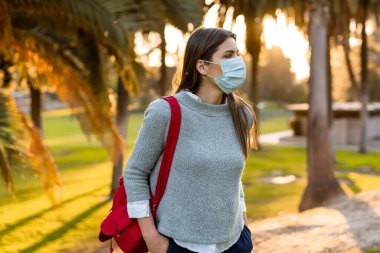 Yüz maskesi takan genç bir kadın, sosyal mesafeler yüz koruması takan insanlardan izole edilmiş..