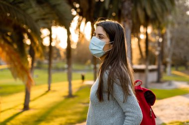Yüz maskesi takan genç bir kadın, sosyal mesafeler yüz koruması takan insanlardan izole edilmiş..