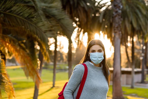 Young woman outdoor wearing face mask, social distancing isolated from other people wearing face protection.