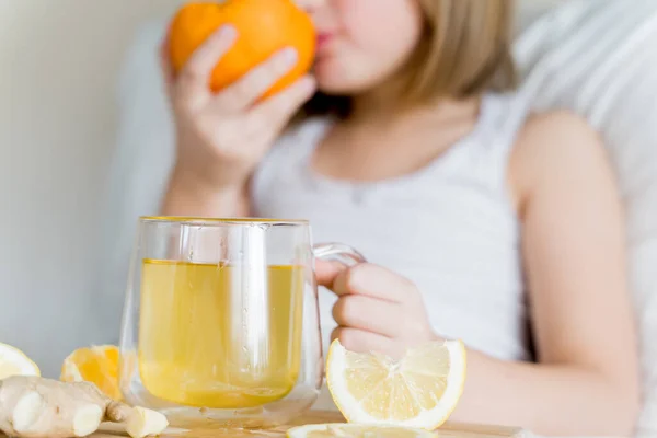 Sick girl in bed tastes half of orange.Cup of antipyretic drugs. Colds,flu.Tea with citrus vitamin C,ginger root,lemon.Wooden tray.Home self-treatment.Medical quarantine therapy. Covid-19,coronavirus.