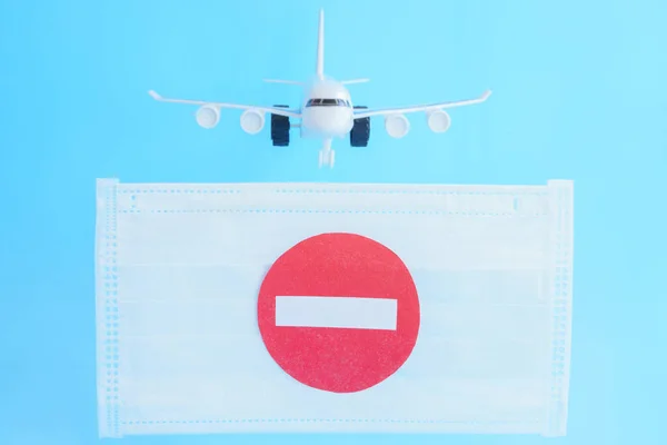 Plane flying in blue sky ran into face mask barrier with stop sign.Flight prohibition,closing of borders. Quarantine of pandemic coronavirus covid-19. Cancellation of business trips,travel vacations.