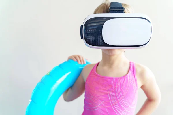 Girl in virtual reality glasses girl, pink swimsuit,blue swimming circle.Online tour to sea,beach.Failed vacation.Travel,tourism around world from home.Self-isolation, quarantine coronavirus covid-19.