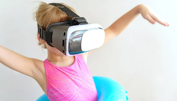 Girl in virtual reality glasses girl, pink swimsuit,blue swimming circle.Online tour to sea,beach.Failed vacation.Travel,tourism around world from home.Self-isolation, quarantine coronavirus covid-19.