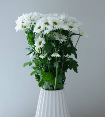 Beyaz bir vazoda beyaz bir çiçek buketi beyaz bir duvara karşı.